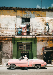 Décoration murale Wandkraft : Personne avec un chapeau à côté d'une voiture rose vintage devant un bâtiment coloré, décoration murale chaleureuse de style rétro. pour un intérieur élégant