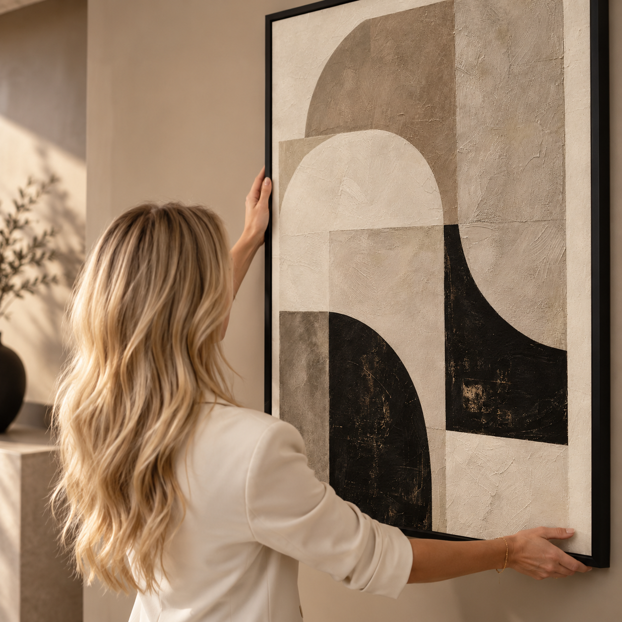 Blonde vrouw hangt een abstract canvas kunstwerk in zwart en beige op