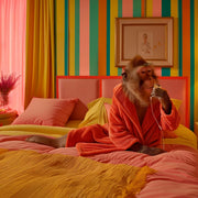 Décoration murale Wandkraft : Singe en tenue orange sur un lit coloré avec un téléphone dans une pièce rayée haute en couleur, œuvre murale moderne de Wandkraft. pour un intérieur élégant