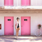 Décoration murale Wandkraft : Femme en veste rose, bigoudis et talons hauts, riant devant des portes de motel roses et un vélo blanc. Œuvre murale Wandkraft de style rétro. pour un intérieur élégant
