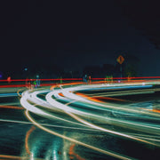 Wandkraft wanddecoratie: Kleurrijke lichtsporen op een donkere, natte straat, dynamisch en sfeervol weergegeven als wanddecoratie uit de Travel Stories-serie. voor een stijlvol interieur