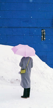 Wandkraft Wanddekoration: Person in grauer Jacke mit rosa Regenschirm im Schnee vor blauer Wand, moderne, stimmungsvolle Wandkraft Wandkunst Land der Aufgehenden Sonne 028. Für ein stilvolles Interieur