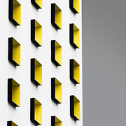 Wandkraft Wanddekoration: Wanddekoration mit weißer Fassade und gelben, rechteckigen Fenstern vor grauem Himmel auf Dibond, modernes und klares Design. Für ein stilvolles Interieur